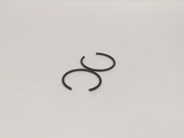 On a white surface, there are two black metal rings; one is in its complete form and the other is partially open.
