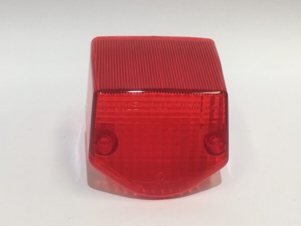 El Plástico piloto trasero es una cubierta de luz trasera roja, rectangular y con una textura acanalada. Tiene dos orificios cerca de la base y se presenta sobre un fondo liso, siendo una pieza de repuesto duradera y elegante para los entusiastas de los vehículos.