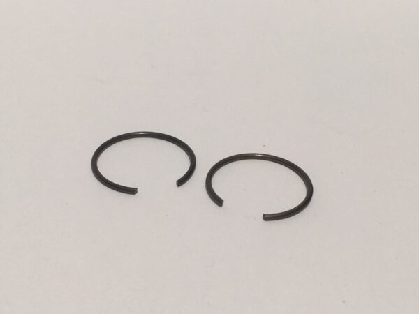 A pair of small, open-ended piston pin circlips resting on a plain white surface.