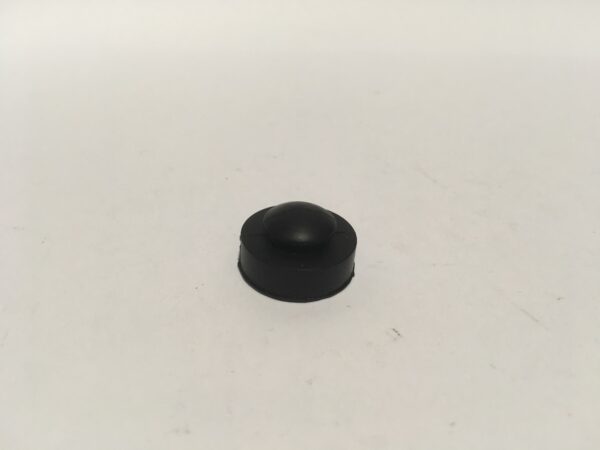 Sobre una superficie blanca y lisa se encuentra una pequeña goma protectora de forma redonda, diseñada para cubrir el escape lateral, que tiene una parte superior en forma de cúpula.
