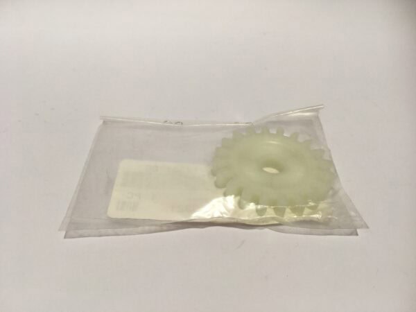 Una bomba de aceite de piñón arrastre, similar a un engranaje de plástico transparente, está envuelta en una bolsa de plástico clara y colocada sobre una superficie blanca lisa.