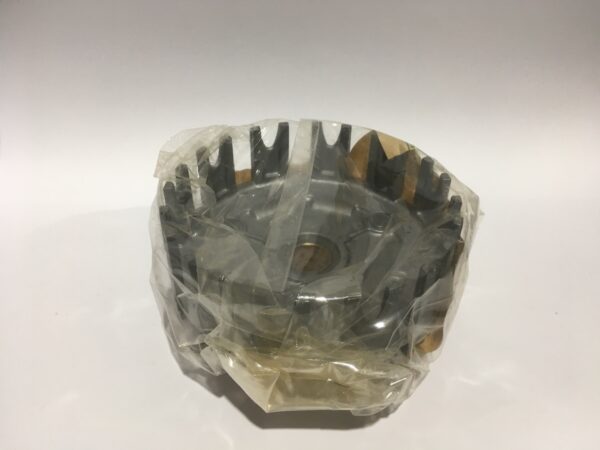 Un componente metálico del motor, tal vez un ventilador de enfriamiento o un rotor, envuelto parcialmente en plástico transparente sobre un fondo simple. Su diseño intrincado y brillo metálico se asemeja a una corona de embrague.