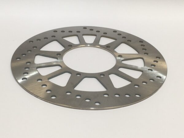 A metal brake disc with a hole in the center and several perforations rests on a flat surface.