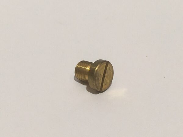 Sobre una superficie blanca descansa con elegancia un tornillo de cabeza plana de latón, que recuerda a un "tapón del segundo cuerpo de un carburador".